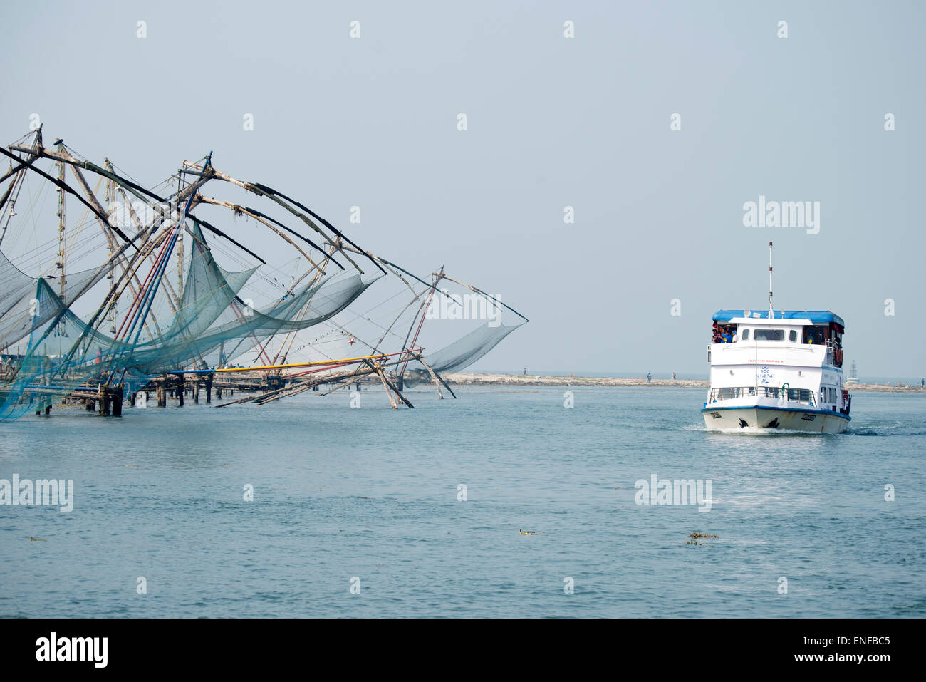 Un bateau de banlieue passant par une rangée de 8 filets de pêche chinois avec quelques filets abaissés dans l'eau à fort Cochin, Kochi, Kerala, Inde les filets sont abaissés Banque D'Images