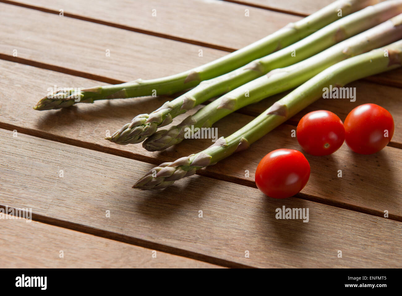 Asperges et tomates cerises rouges sur une table en bois Banque D'Images