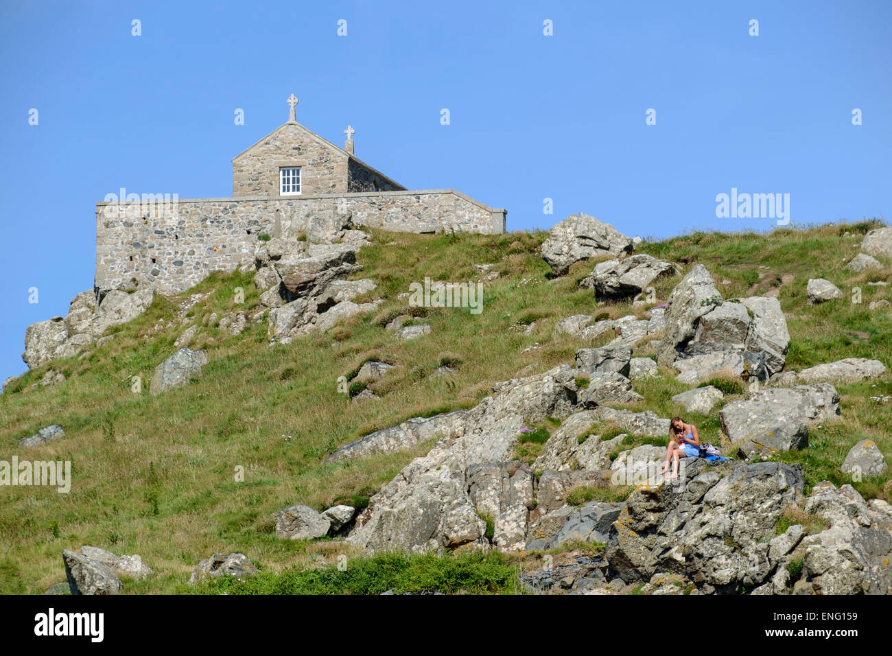 St Ives, Cornwall : jeunes femmes en robe bleue se détendre sur des roches à St Ives en Cornouailles avec chapelle St Nicolas derrière Banque D'Images