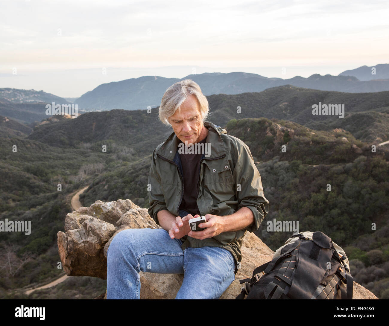 Older Caucasian man using cell phone on rocky hilltop Banque D'Images