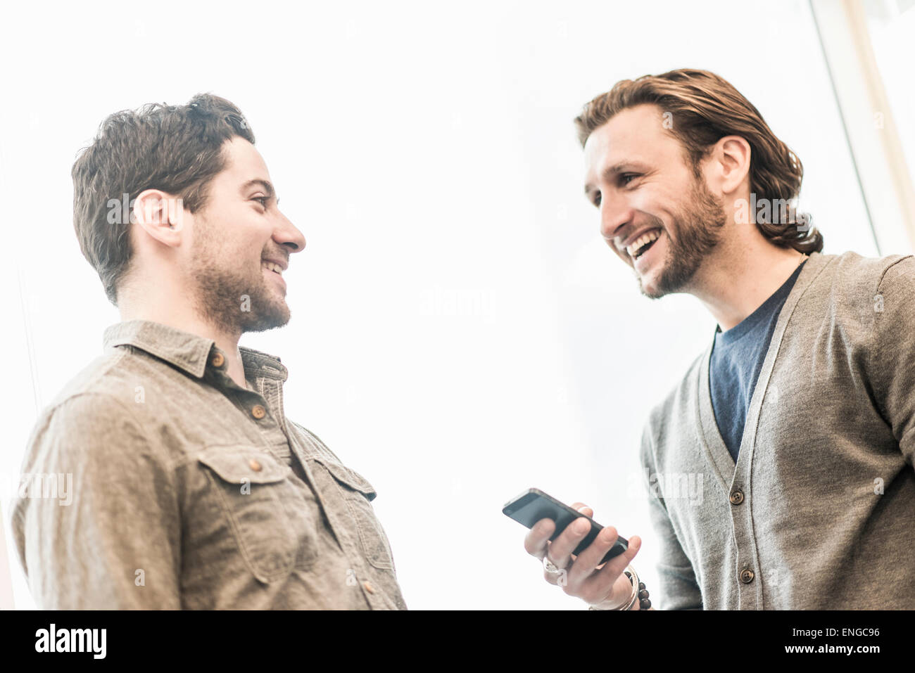 Deux hommes souriant, l'un tenant un téléphone intelligent. Banque D'Images