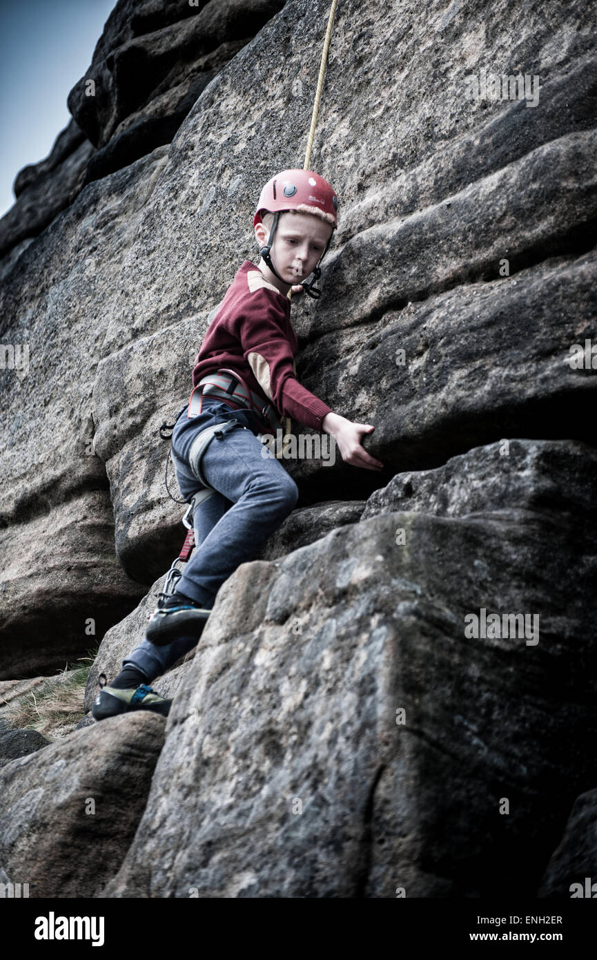 Un jeune garçon escalade à Stanage Edge dans le Peak District Banque D'Images