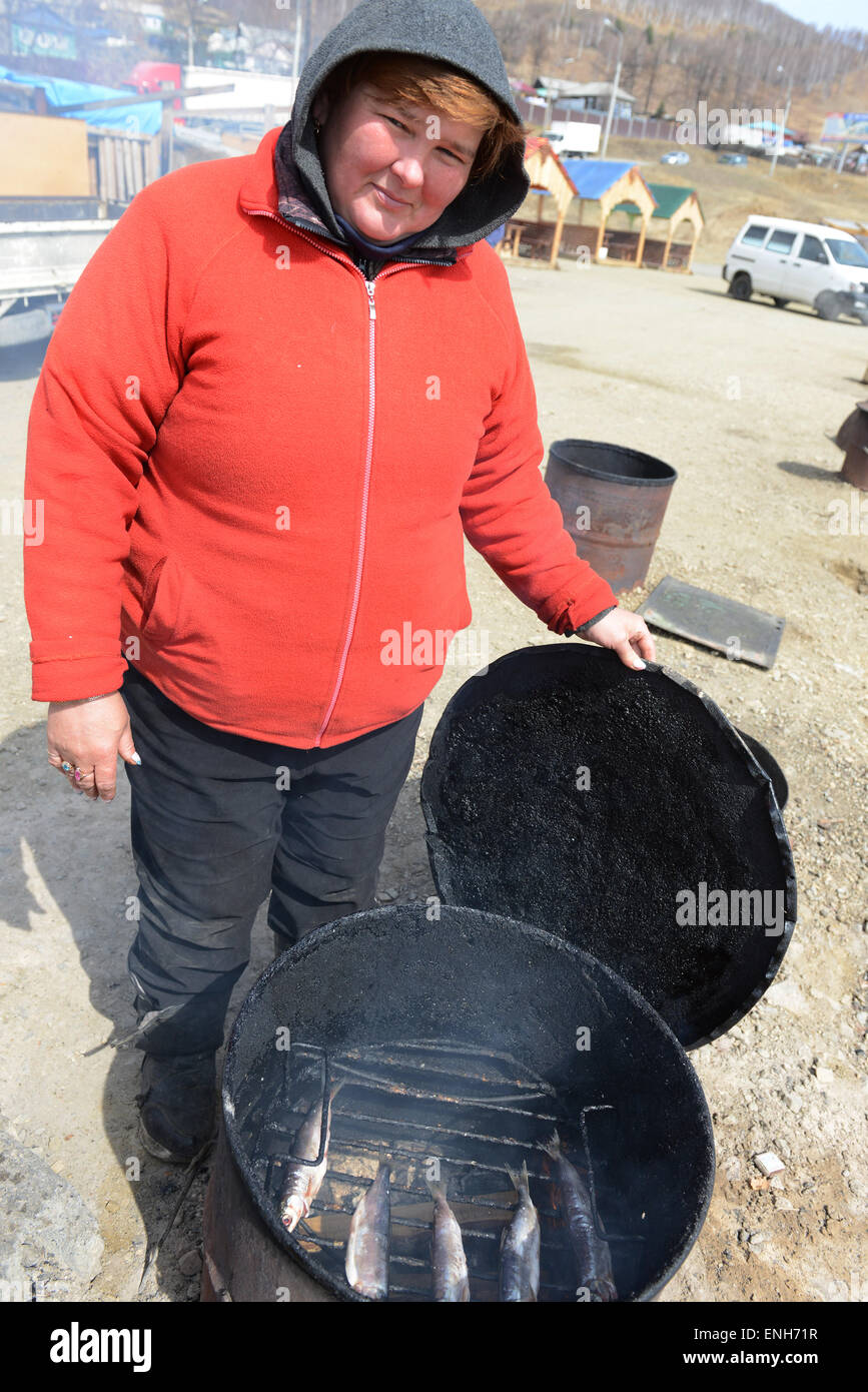 Une femme Russe fumeurs poisson Omul Baïkal ( la famille de corégone ). Banque D'Images