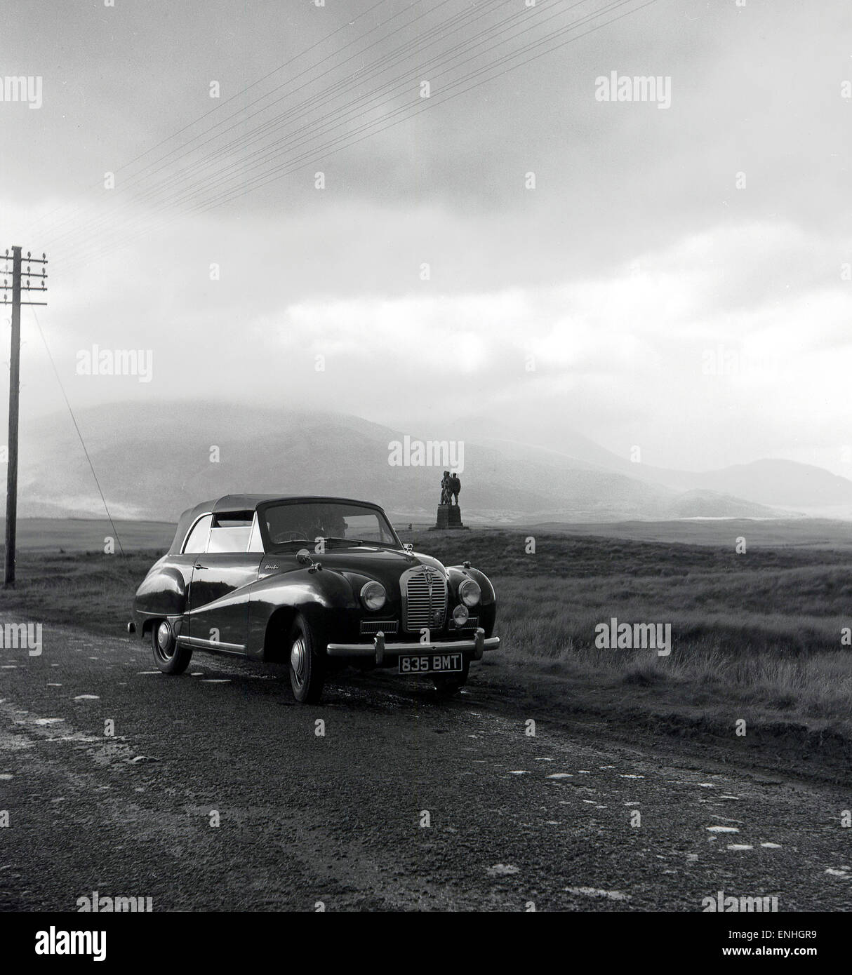 Historique, années 1950, Austin Morris voiture garée sur une route à Fort William, les highlands écossais, avec le mémorial Commando dans l'arrière-plan. Banque D'Images