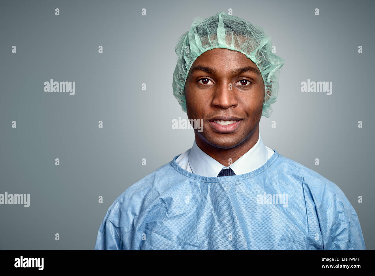Beau jeune homme africain médecin ou infirmière dans scrubs et un chapeau de la stérilité à la recherche directement sur la caméra sur un fond gris, Banque D'Images