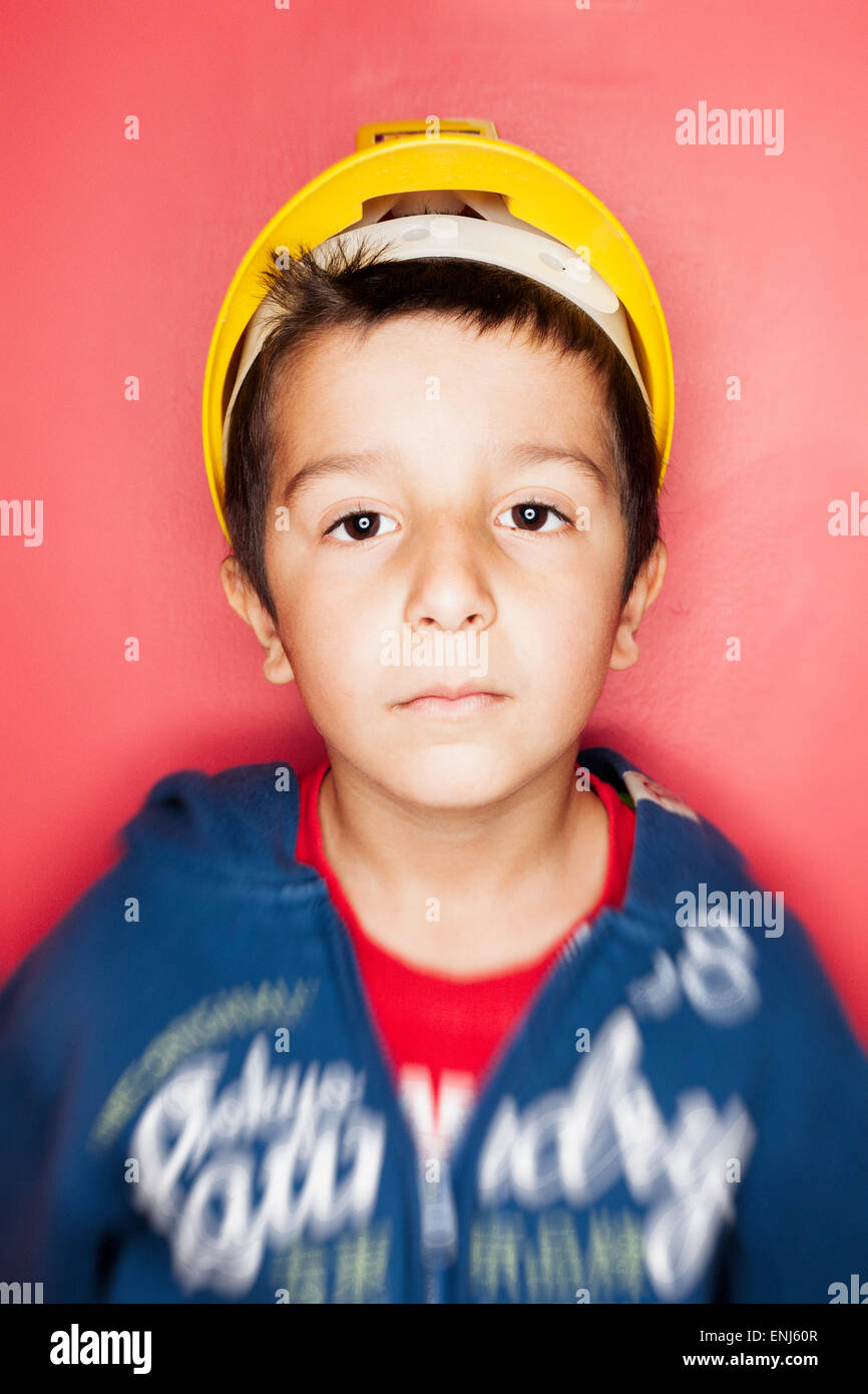 Boy,7,in hard hat contre mur rouge Banque D'Images