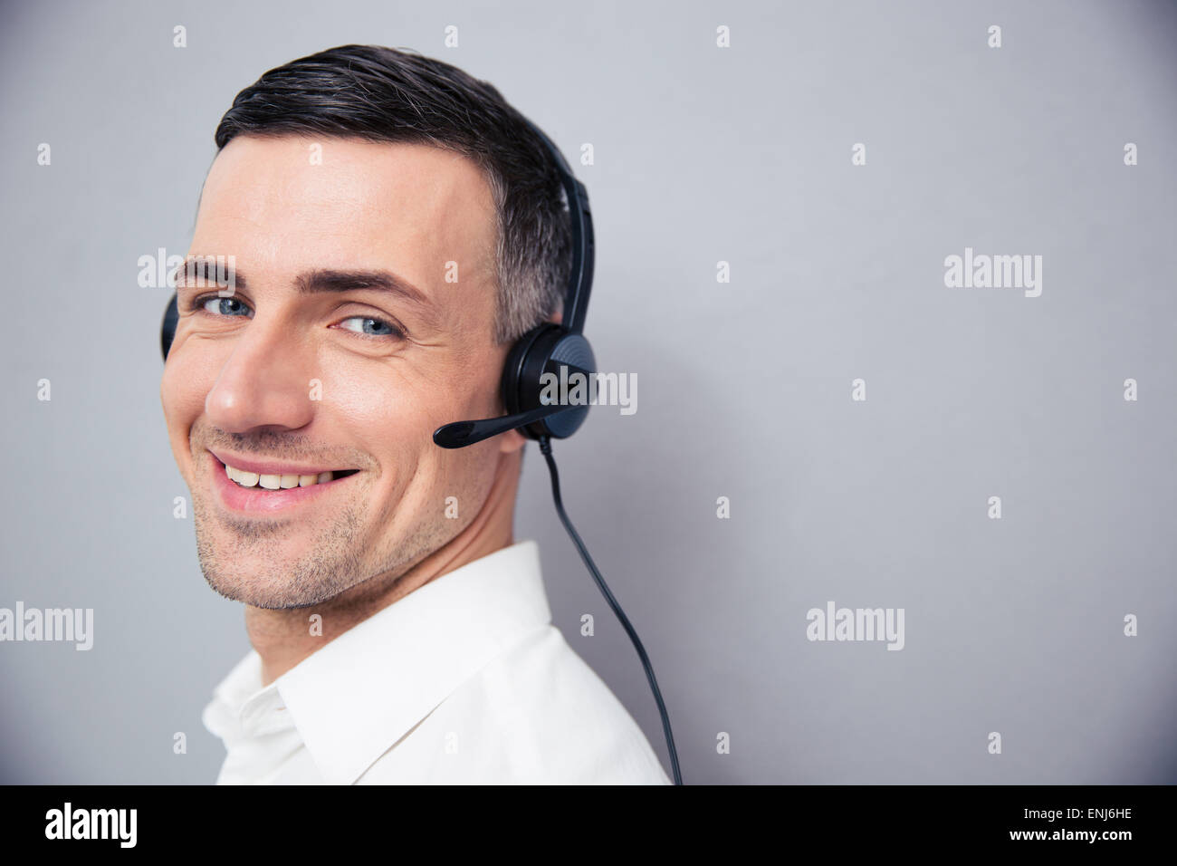 Cheerful businessman in headphones debout sur gray backgorund et looking at camera Banque D'Images