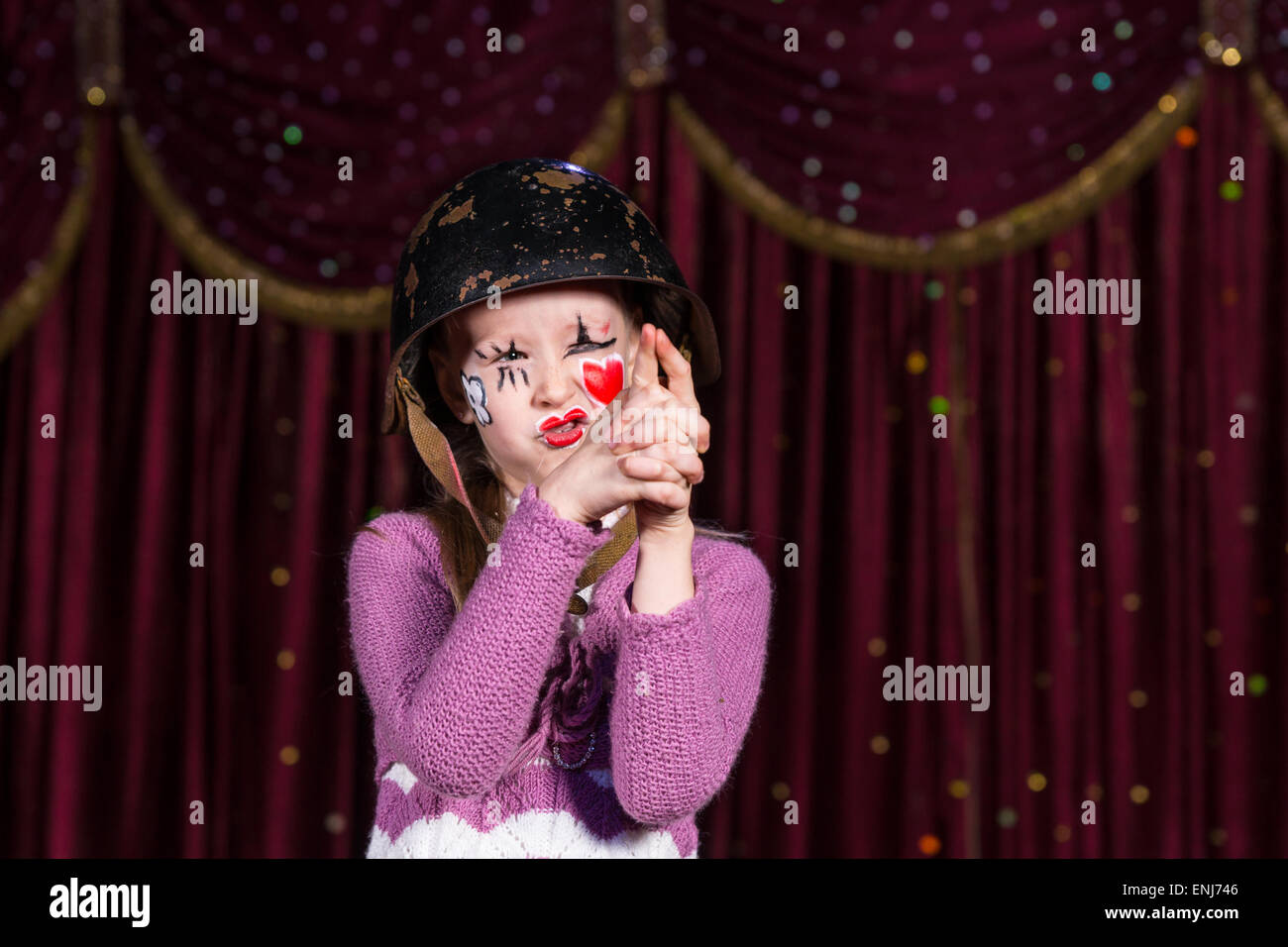 Jolie fille avec vieux casque et avec un cœur rouge peint sur le visage, faisant semblant d'avoir un fusil dans un jeu conceptuel au sujet de la guerre, d'amour et d'innocence. Banque D'Images