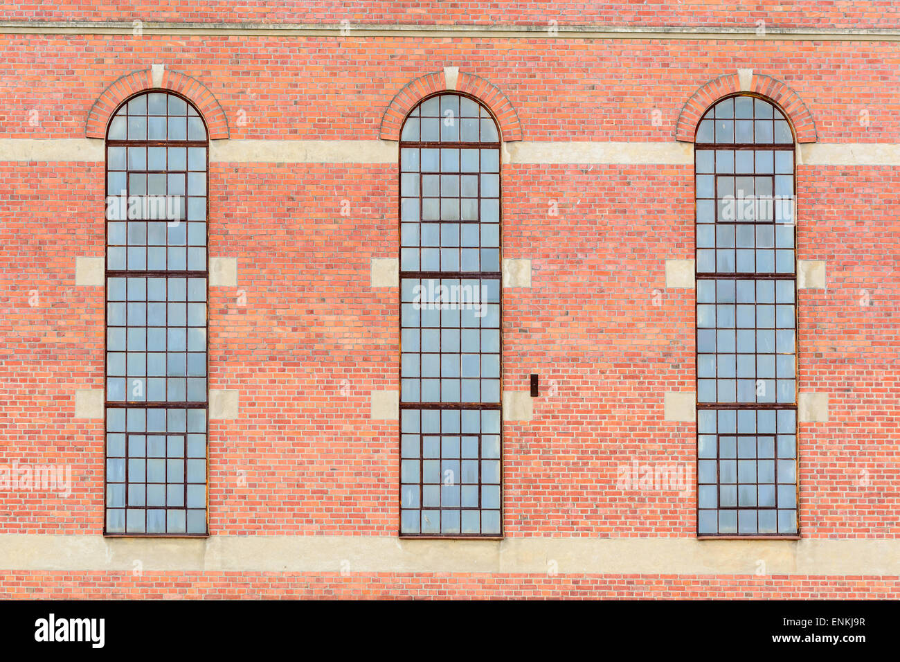 Vieux bâtiment en brique dans une zone industrielle. Trois fenêtres en verre avec des arches sur le dessus. Banque D'Images