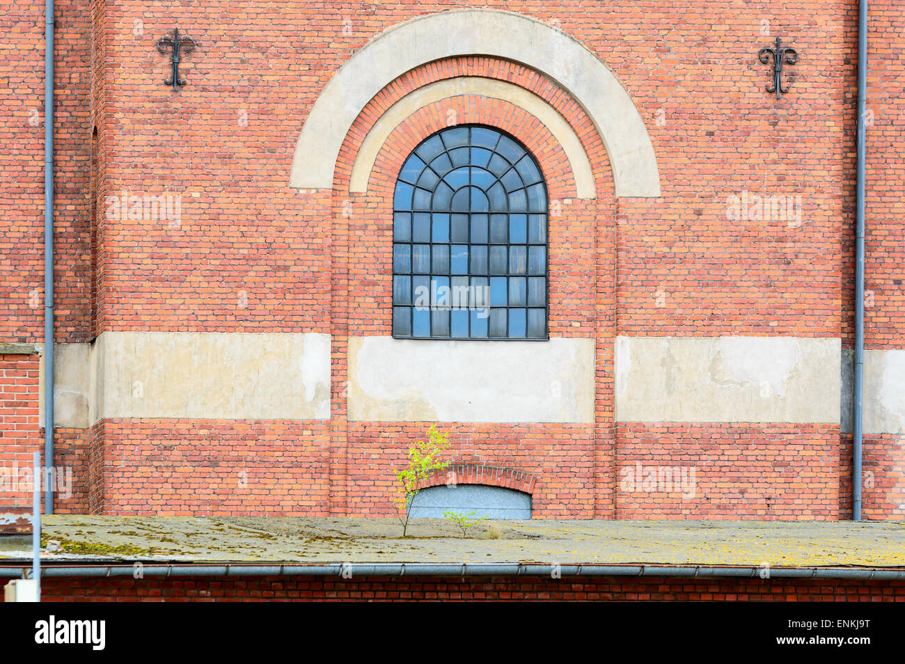 Vieux bâtiment en brique dans une zone industrielle. Un bon verre fenêtre avec arche en pierre au-dessus de lui. Petit arbre commencent à pousser sur le toit de bui Banque D'Images