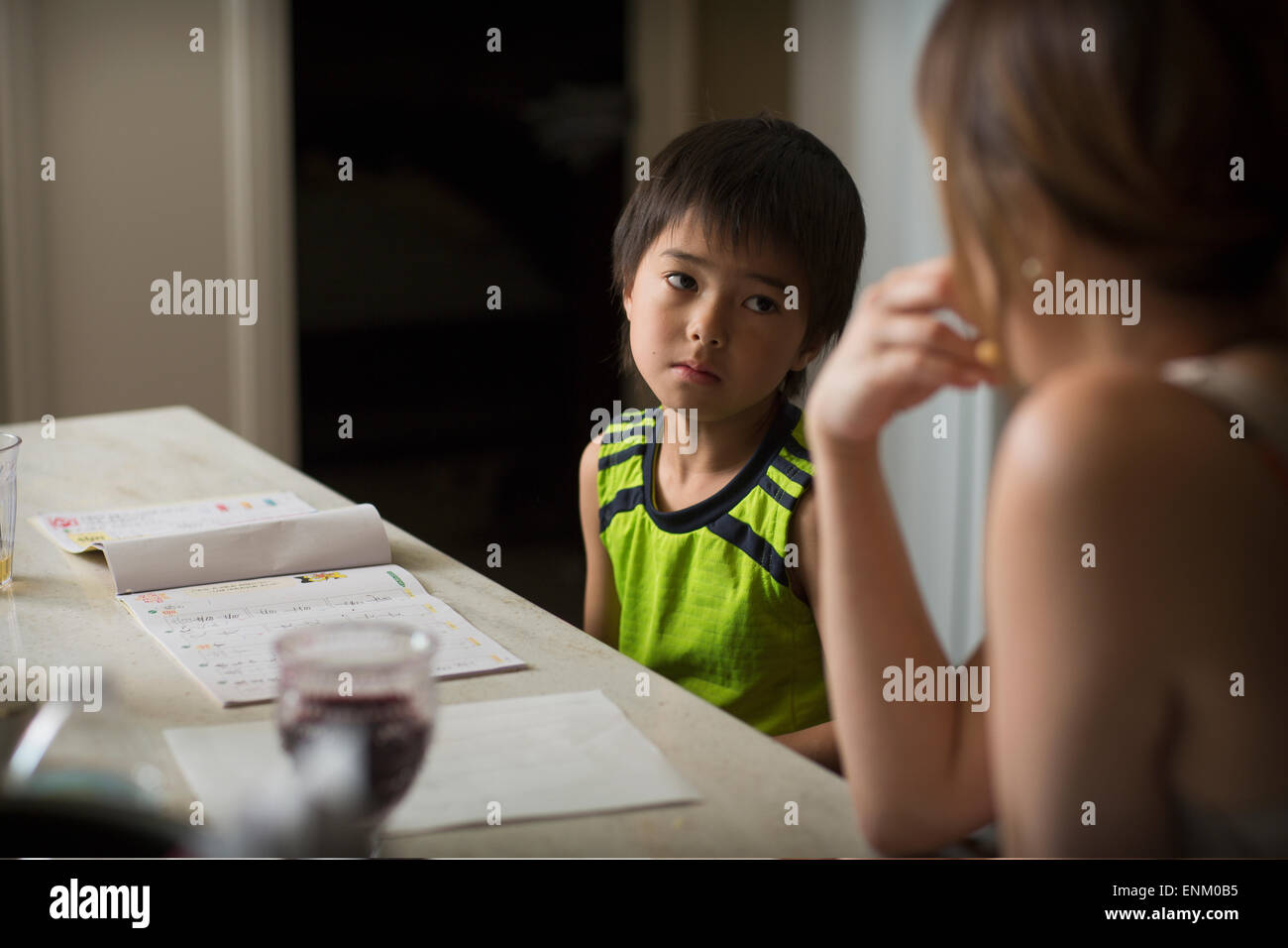 Un garçon Japonais Japonais études devoirs dans une cuisine comme sa maman regarde. Banque D'Images