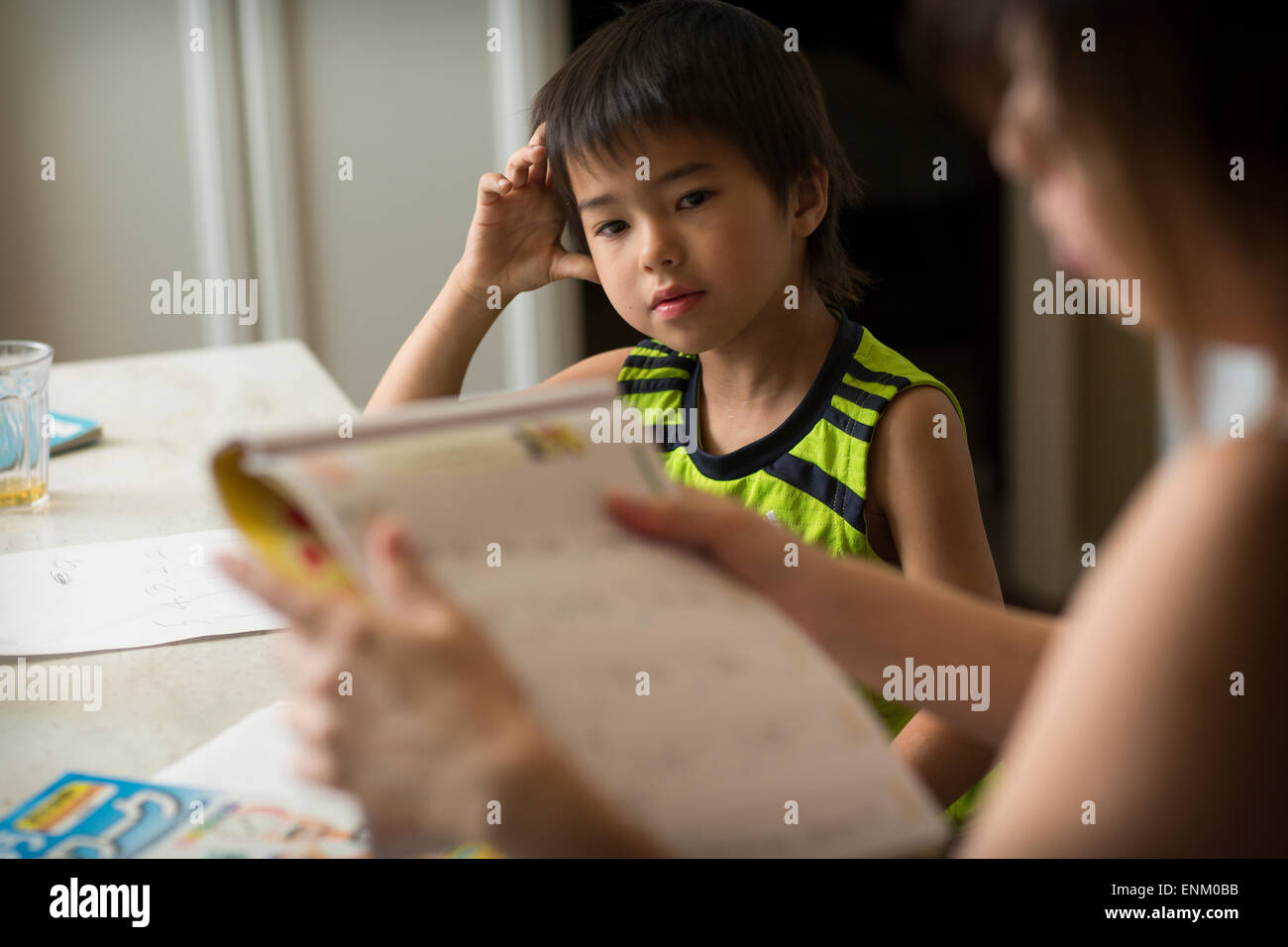 Un garçon Japonais Japonais études devoirs dans une cuisine comme sa maman l'aide. Banque D'Images