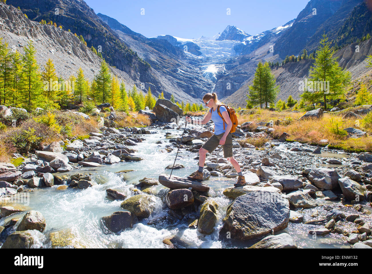 Un female hiker est traversée d'un cours d'eau des glaciers dans les Alpes suisses. Banque D'Images