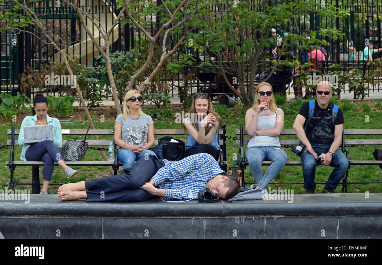 Jeune homme endormi dans Washington Square Park avec spectateurs indifférents. Banque D'Images