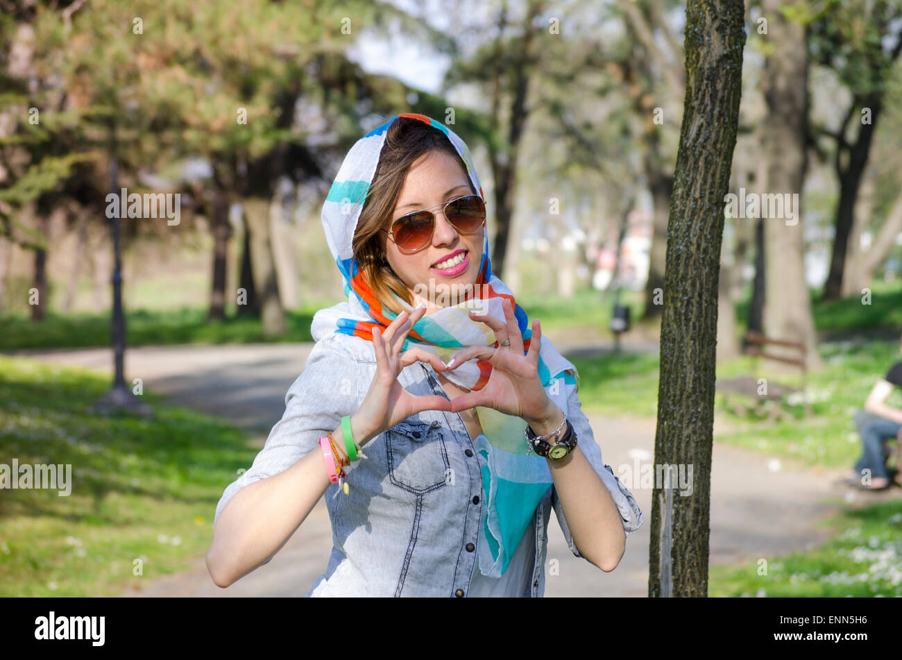 Girl enjoying spring portant un bandana coloré et faisant un heartshape avec ses mains Banque D'Images