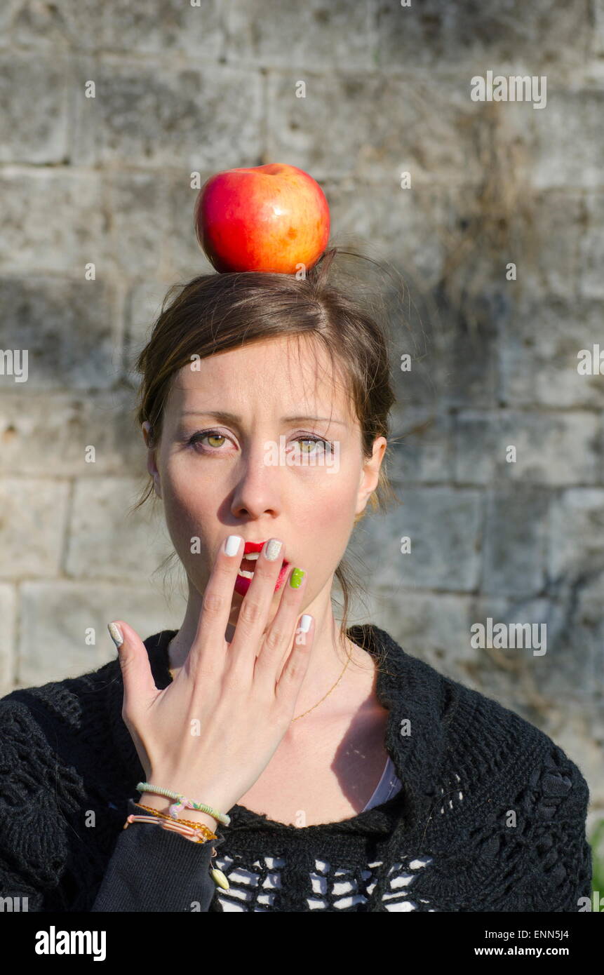 Brunette choqué d'une pomme sur sa tête, posant contre un mur de pierre Banque D'Images