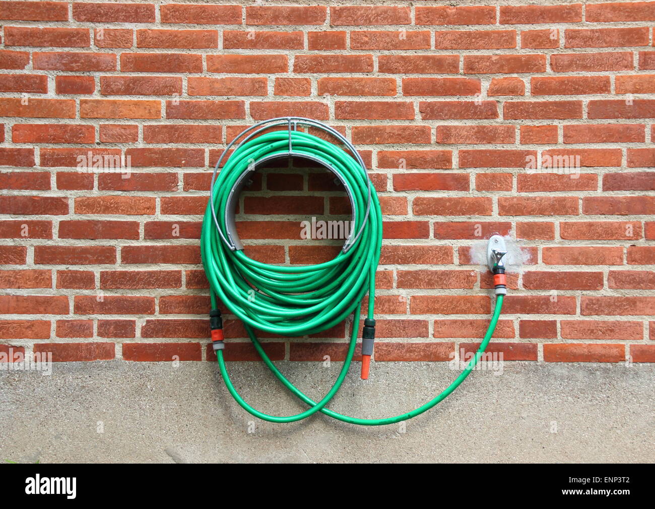 Le flexible d'eau verte hanging red brick wall Banque D'Images