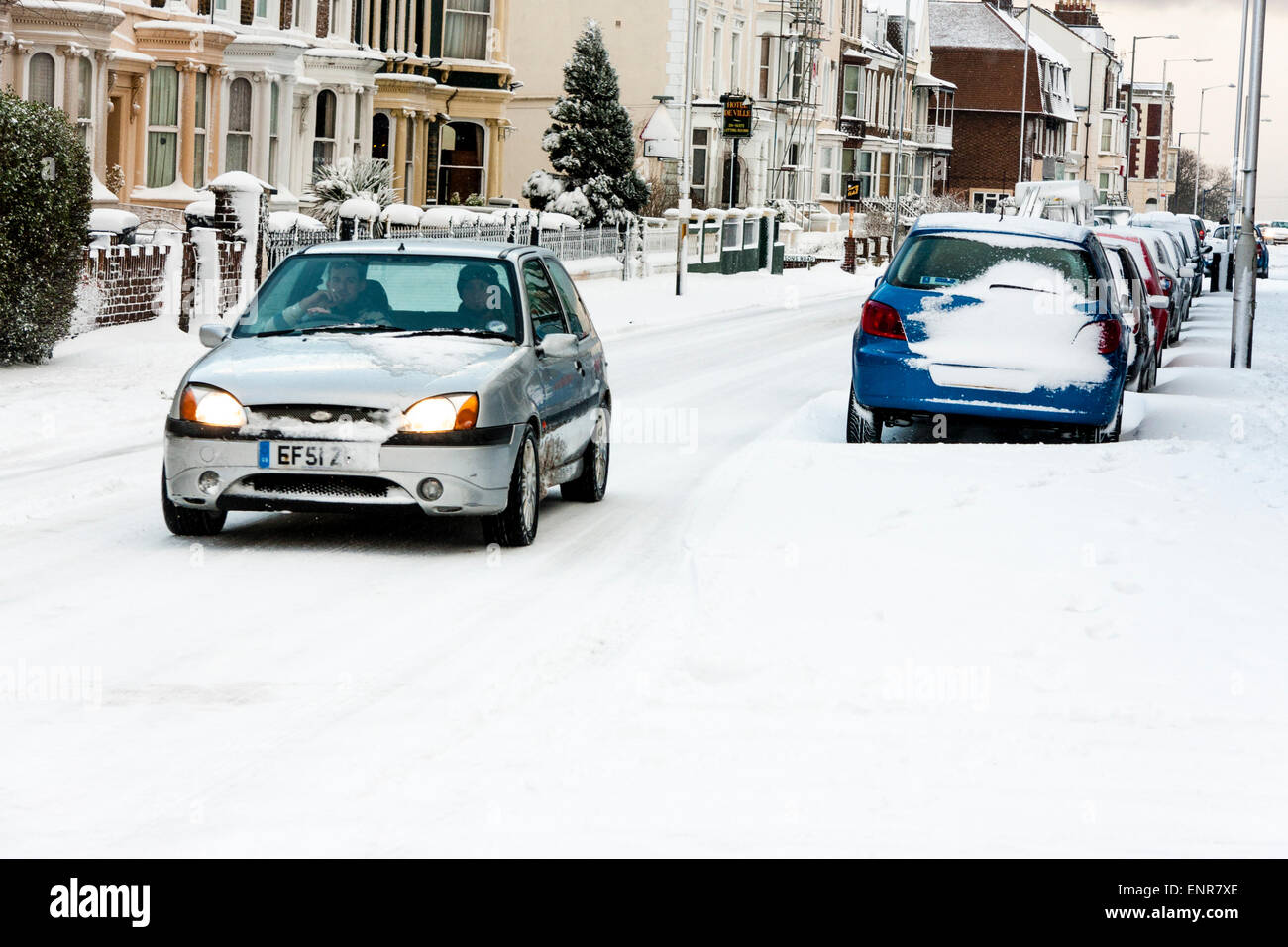 Vue le long de la rue enneigée de Ramsgate en Angleterre après une lourde chute de neige. Voitures garées dans la neige, monovoiture roulant le long de la route. Banque D'Images