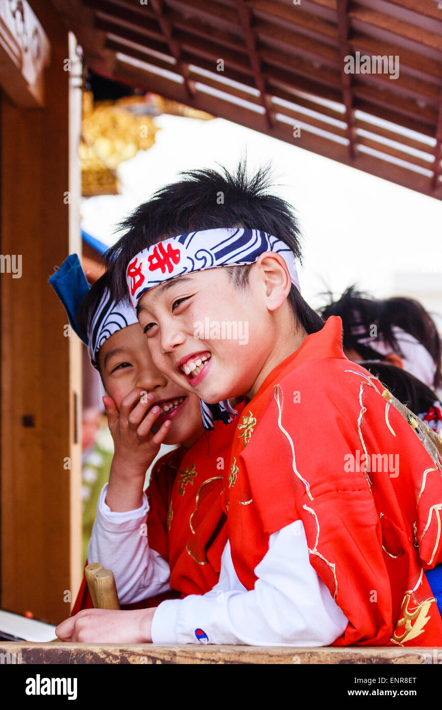Japon, Inuyama. Deux enfants japonais, garçons, 9-10 ans, avec bandeau rose et costume rouge riant tout en étant assis dans un yama, char de carnaval. Banque D'Images