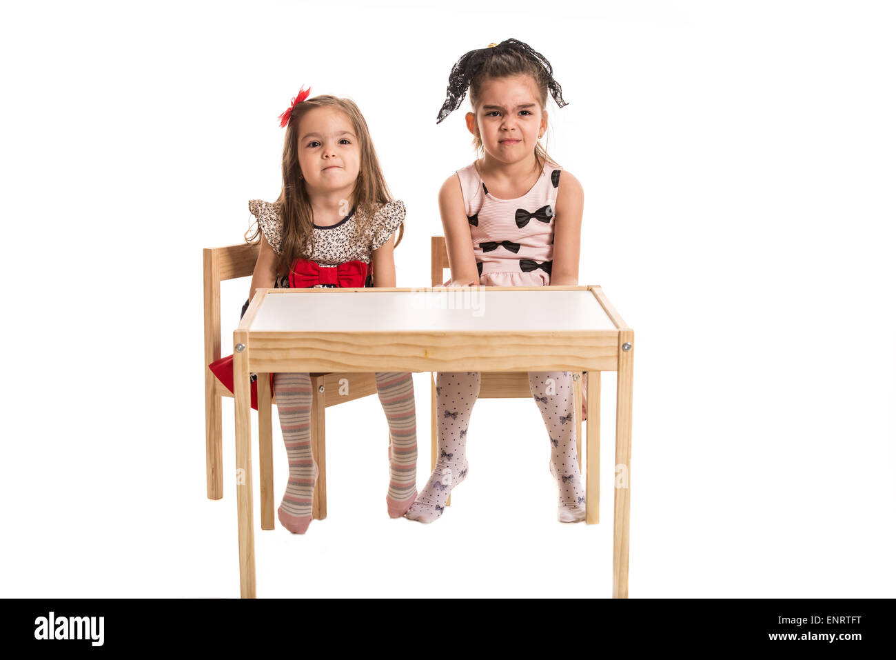 Toute la longueur de deux filles assis à table et faire grimace isolé sur fond blanc Banque D'Images