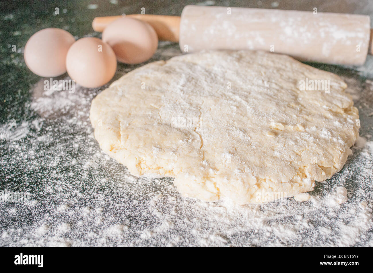 Pâte roulée, oeufs, et d'un rouleau à pâtisserie sur une surface en bois couvert de farine Banque D'Images