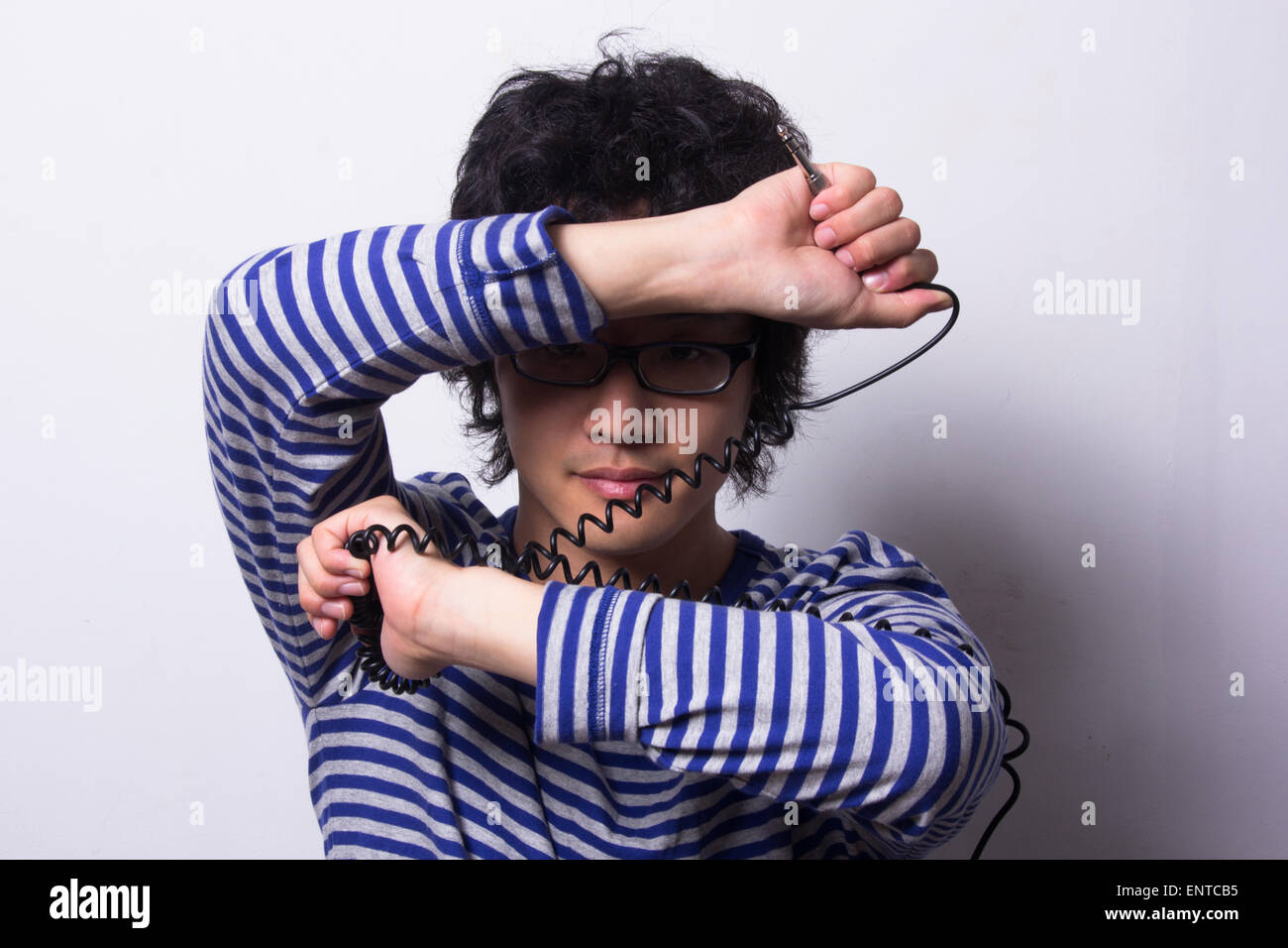 Asian young man looking through arms holding head phone chord Banque D'Images