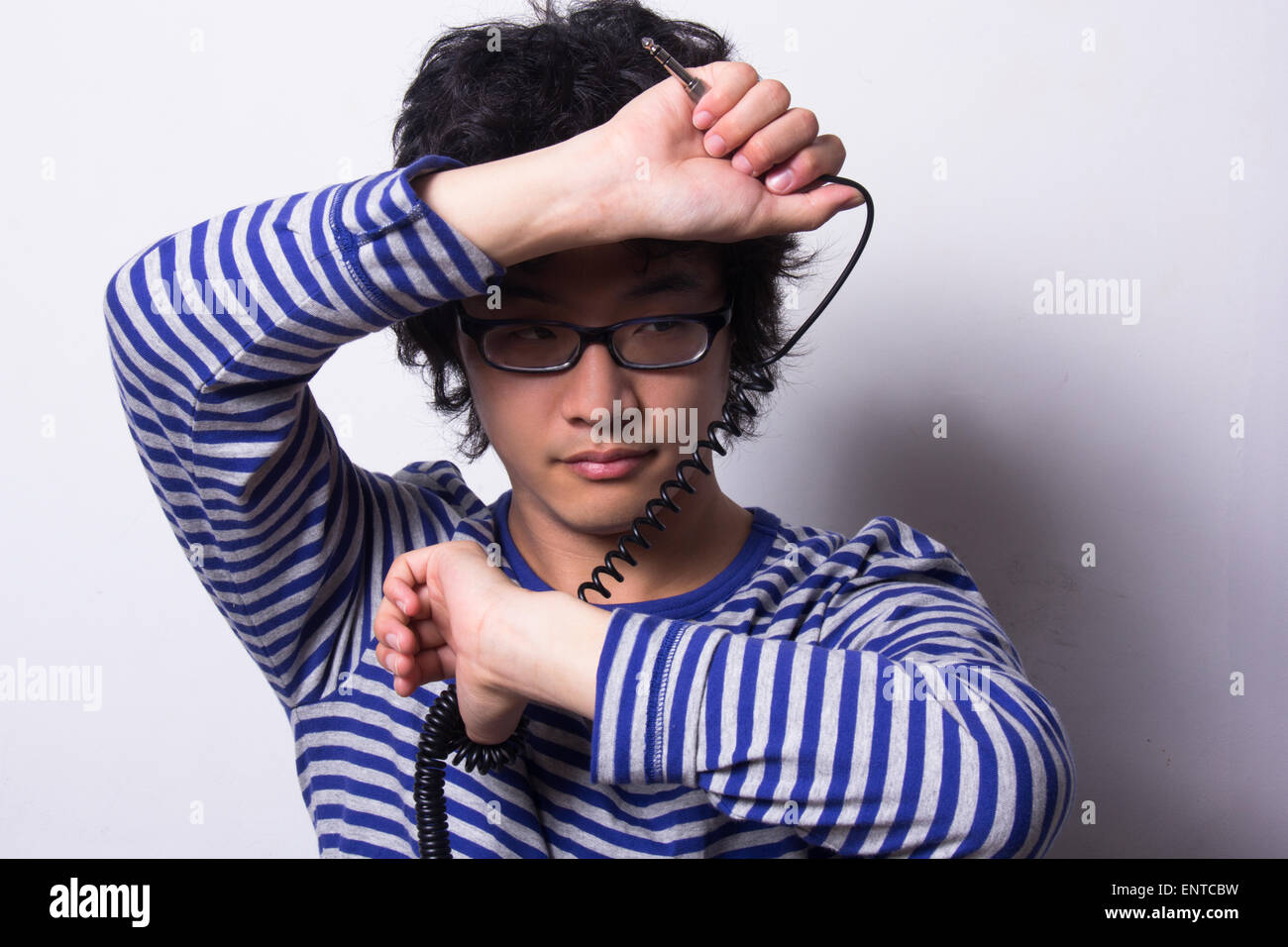 Asian young man looking through arms holding head phone chord Banque D'Images