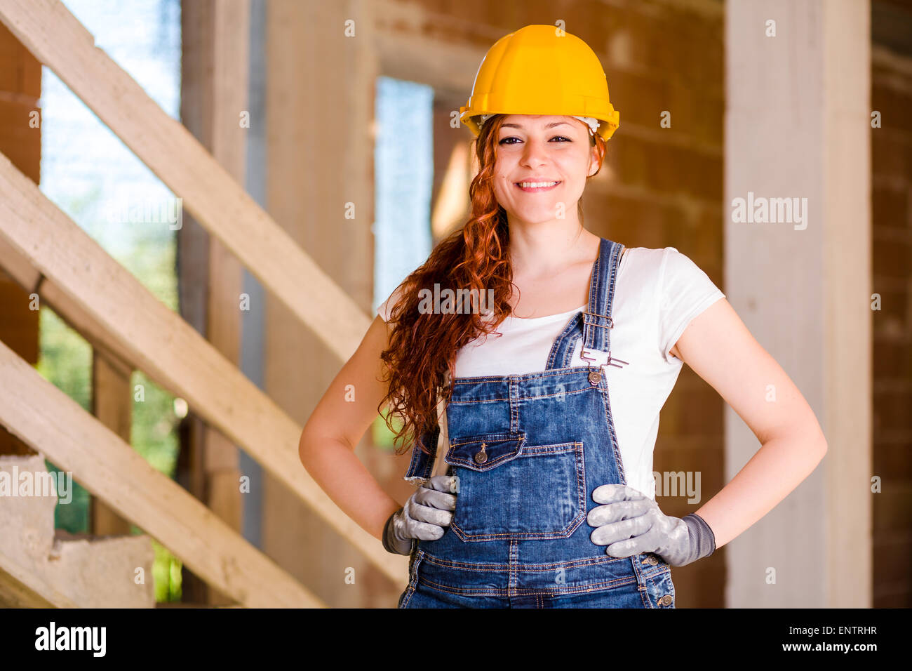 Smiling Woman Charpentier avec bretelles et le casque avec ses mains sur les hanches Banque D'Images