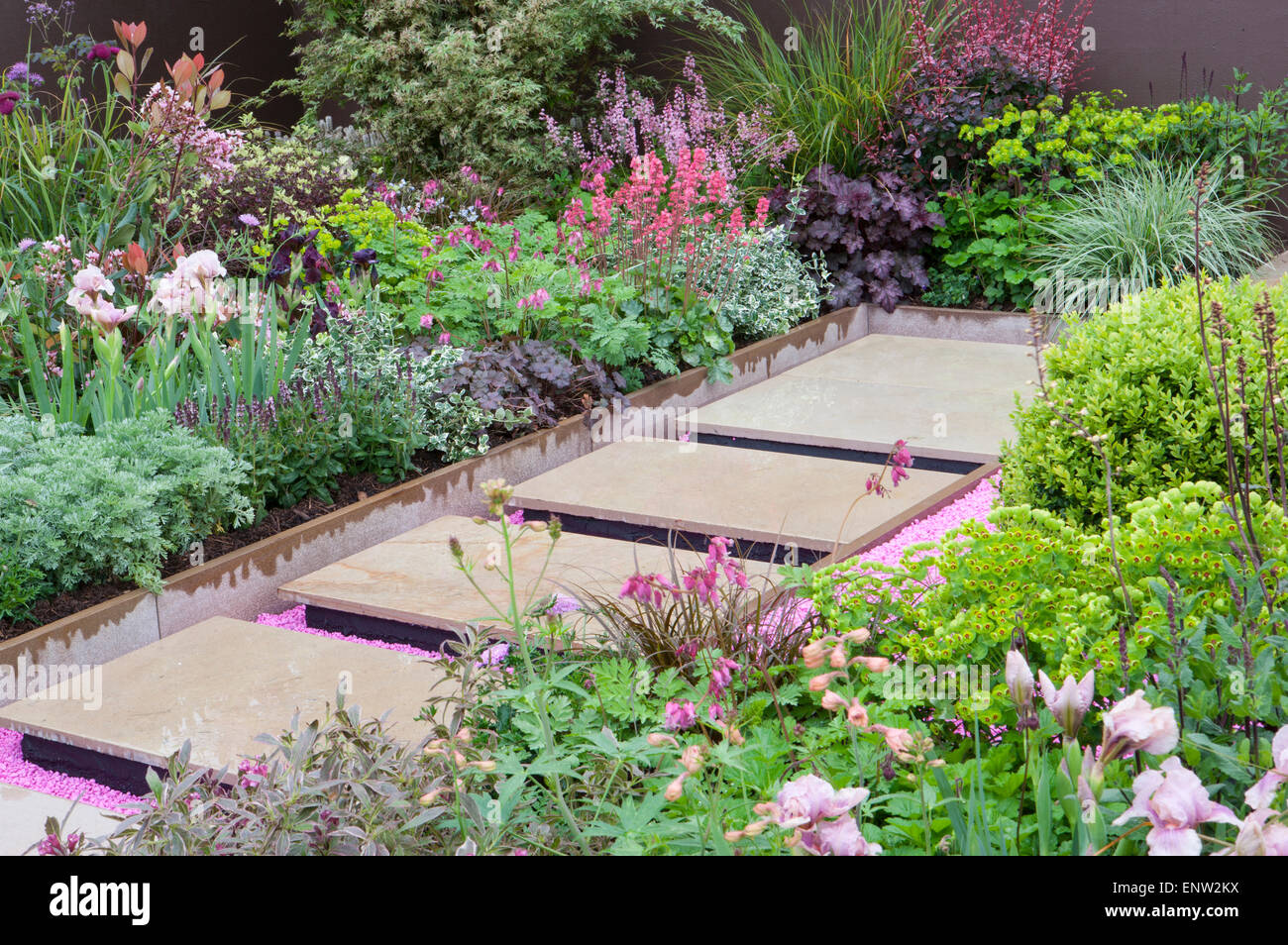 Jardin moderne flottant en pierre pavant sur du gravier rose avec des bordures de fleurs herbacées mixtes - printemps - Angleterre Royaume-Uni - RHS Malvern Spring show Banque D'Images