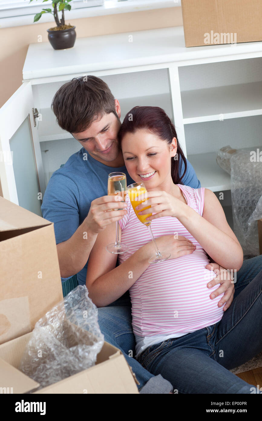 Cheerful couple célébrant la grossesse et dépose avec champagne assis sur le plancher Banque D'Images