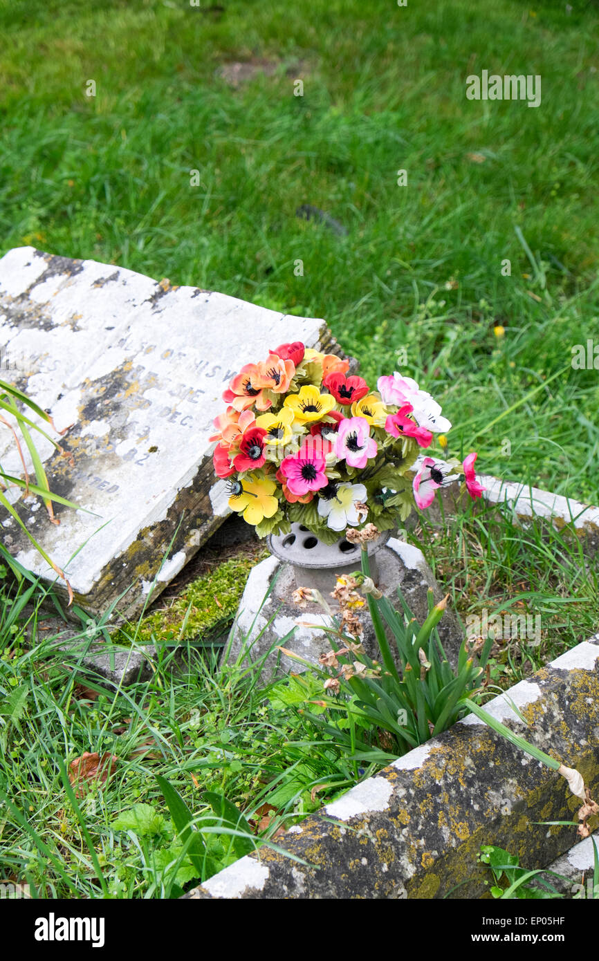 Fausse couleur des fleurs en plastique sur la vieille tombe Banque D'Images