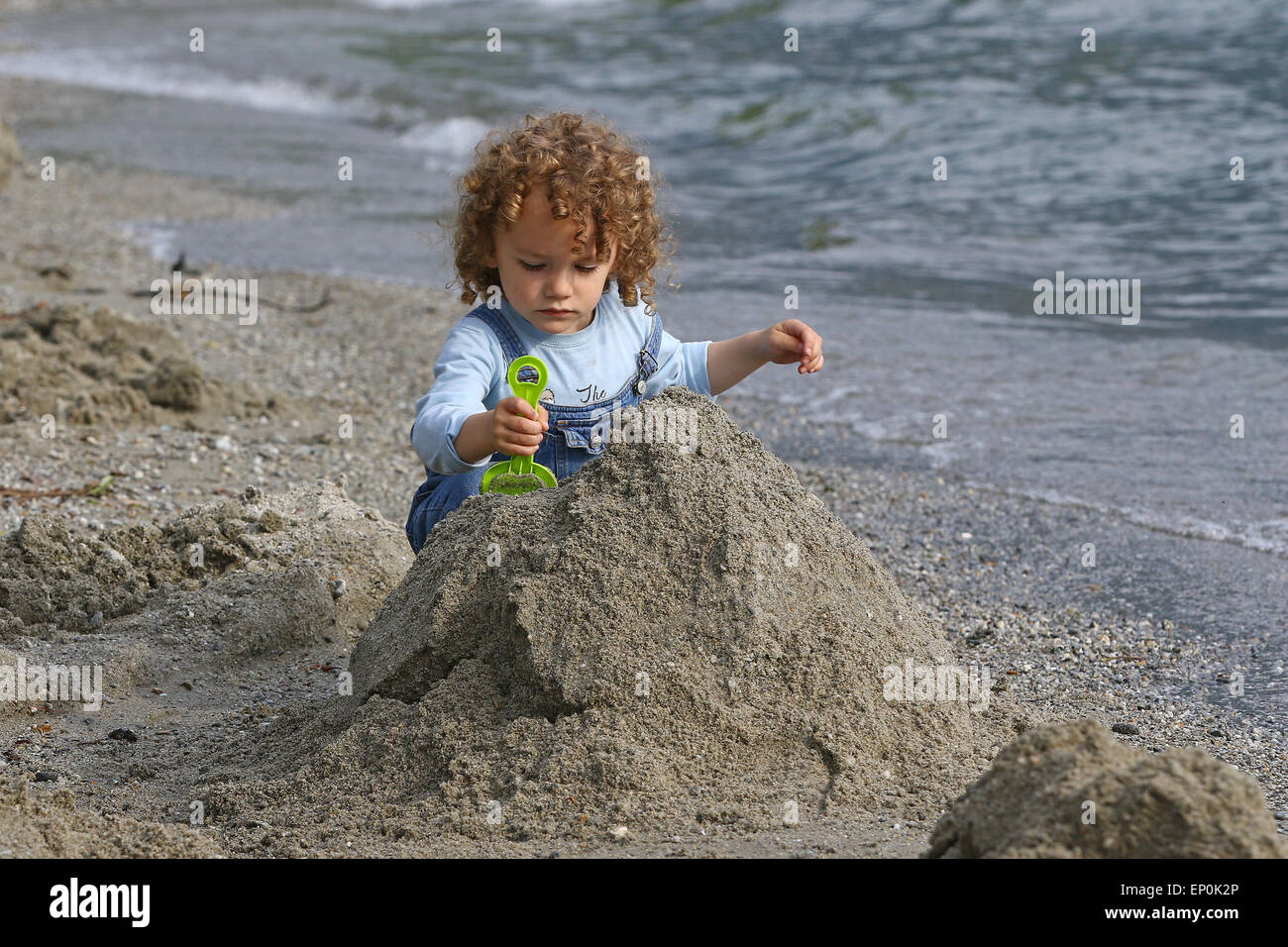 Petit Garçon jouant avec le sable sur une plage au bord du lac Banque D'Images