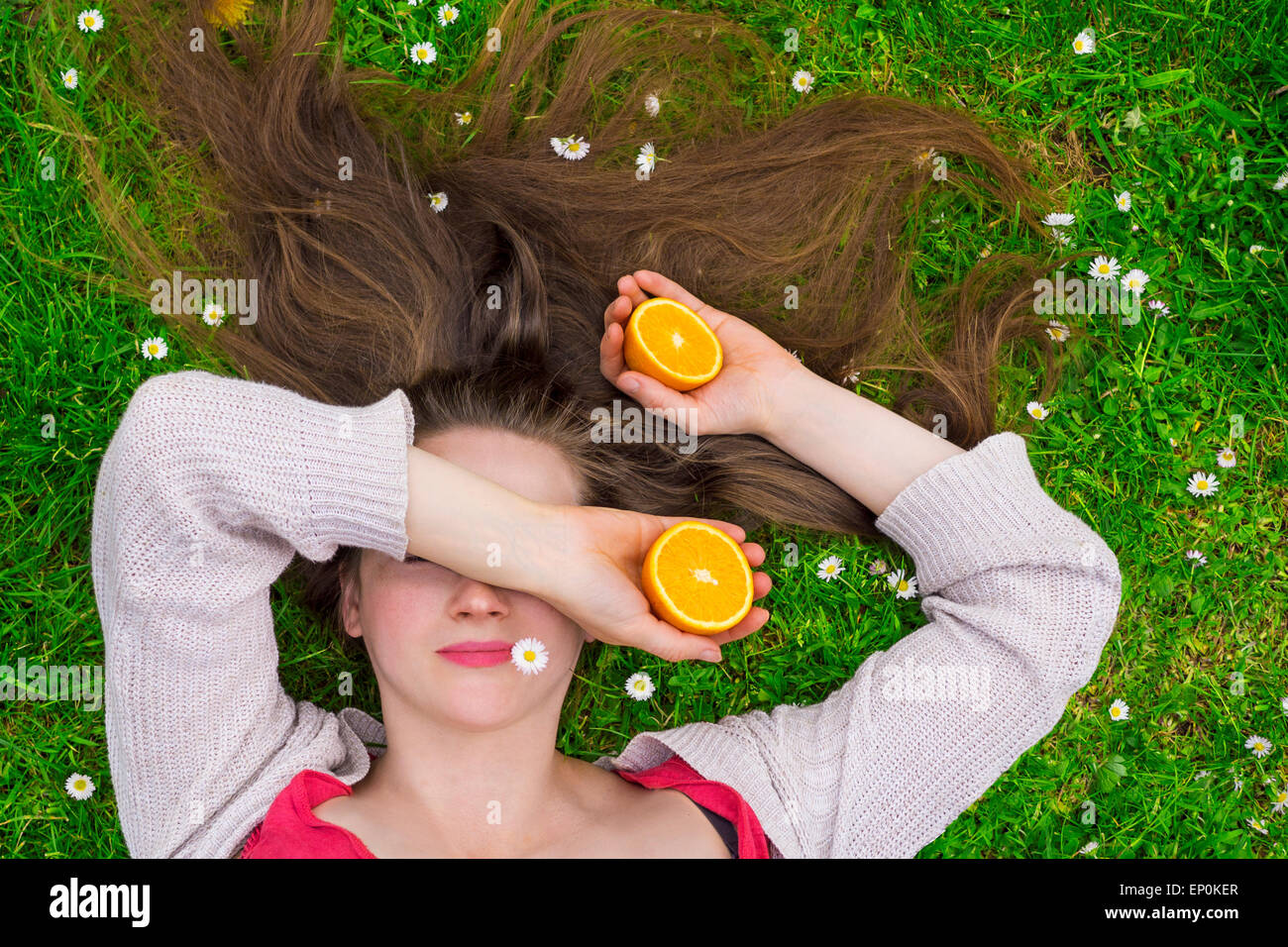 Young woman laying on a grass field holding oranges Banque D'Images