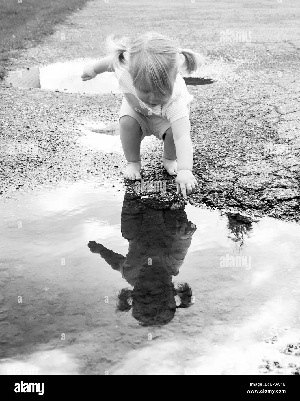 Un enfant découvre son reflet dans une flaque d'eau sur une journée de printemps breezy. Banque D'Images