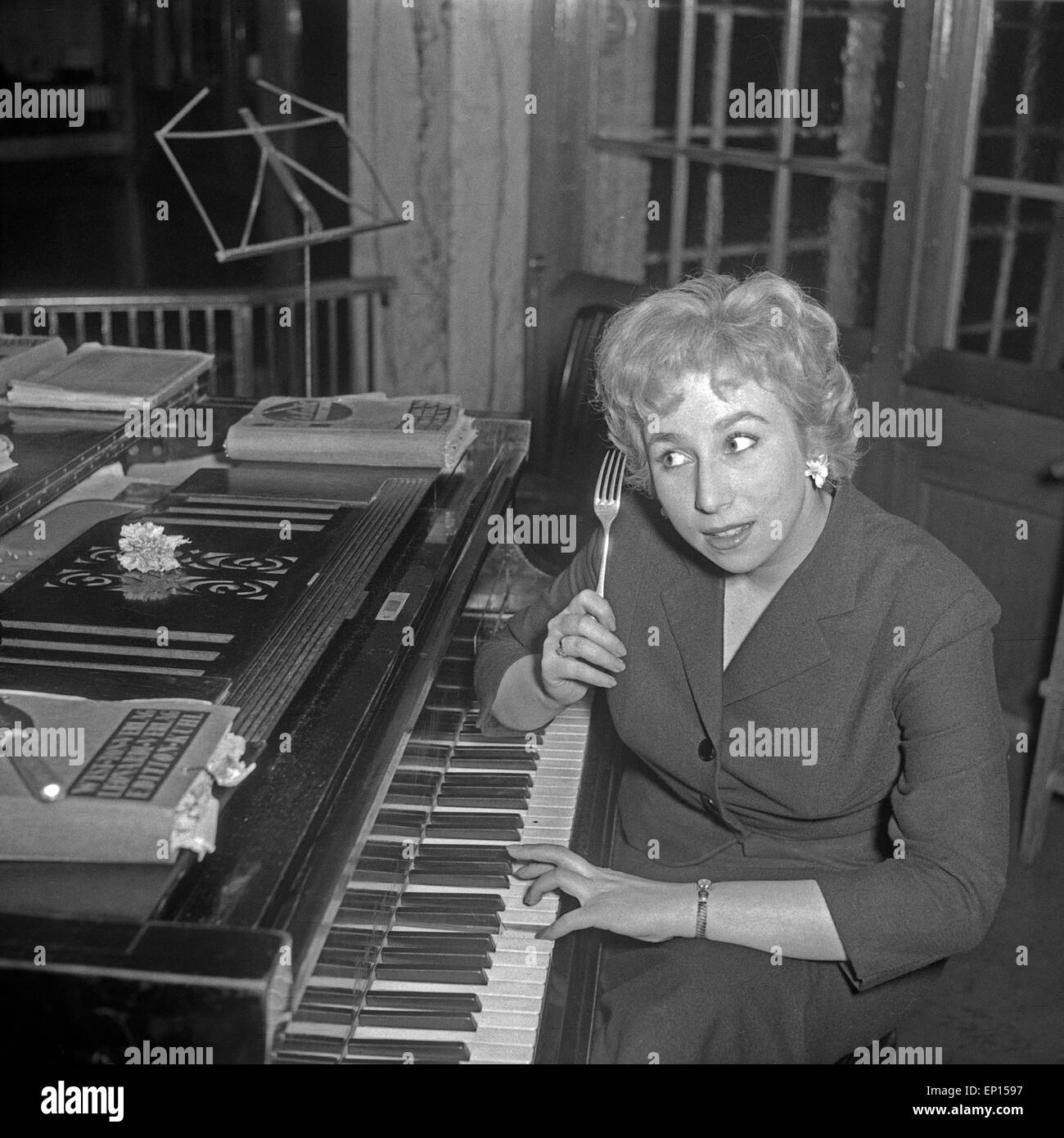 Eine junge Frau sitzt une einem Flügel mit einer Gabel, Deutschland 1950er Jahre. Une jeune femme assise sur un piano avec un f Banque D'Images