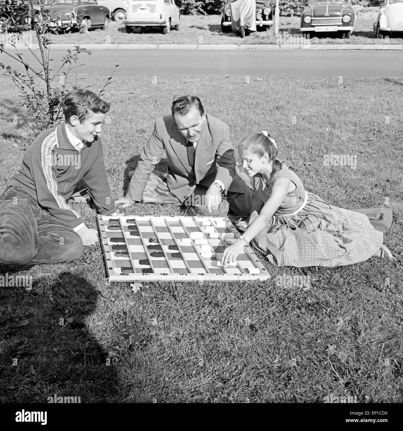 Bringt Ein Mann und einem Jungen Mädchen das bei einem Schachspielen, 1950er Jahre Deutschland. Un homme l'enseignement d'un garçon et une fille Banque D'Images