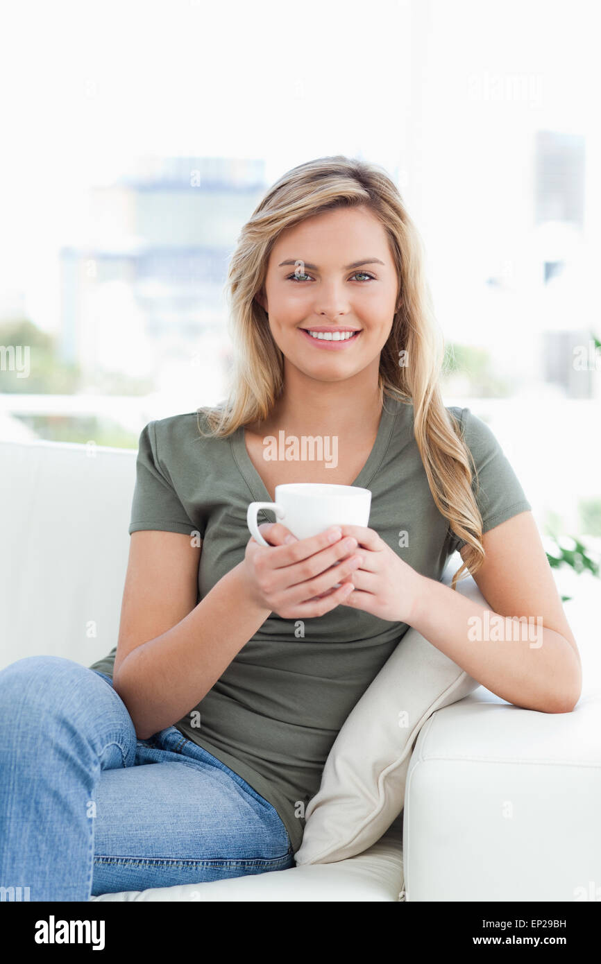 Femme tenant une tasse, souriant alors qu'elle attend avec intérêt les jambes croisées Banque D'Images Femme tenant une tasse, souriant alors qu'elle attend avec intérêt les jambes croisées Banque D'Images