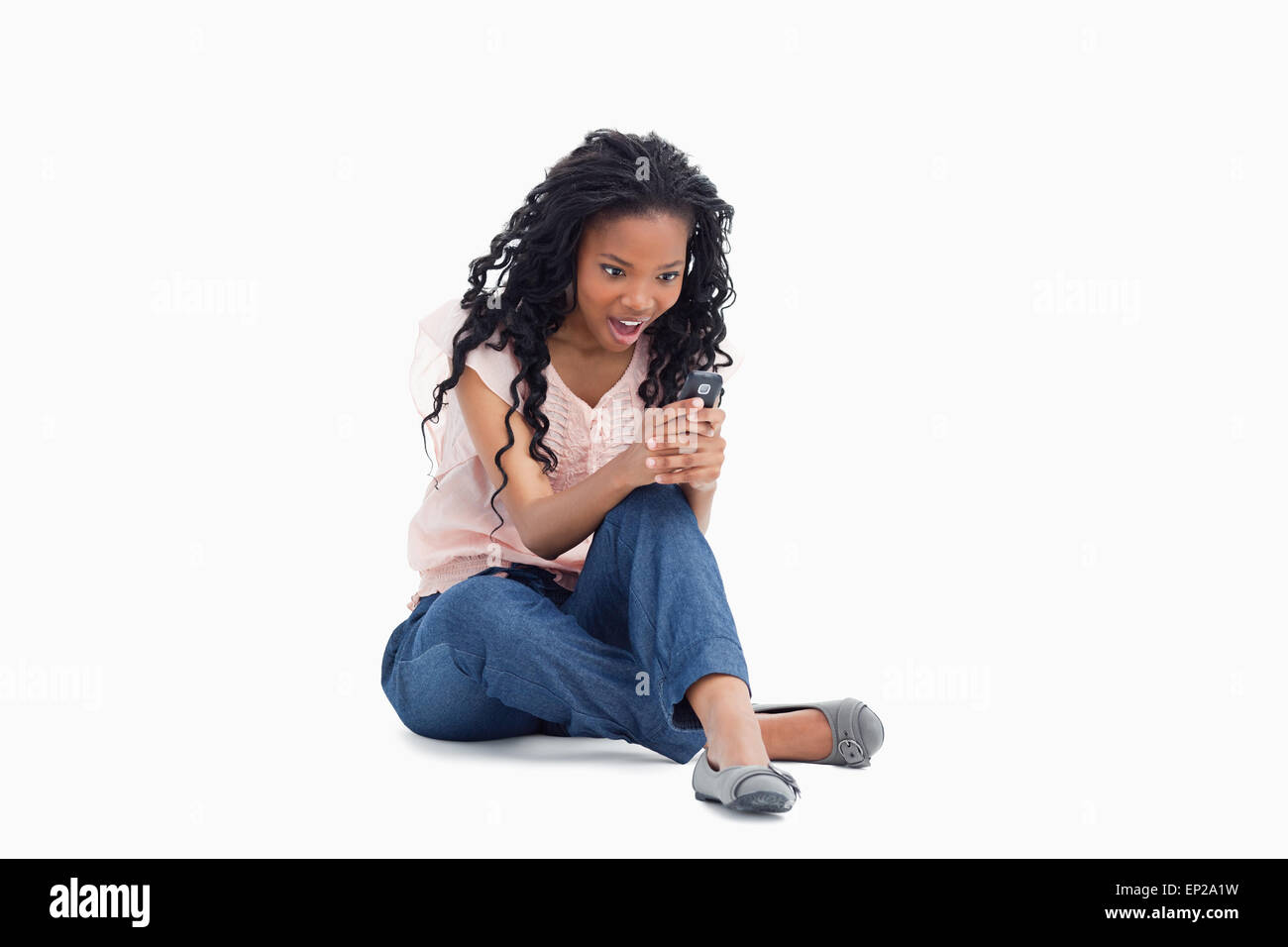 Surpris d'une femme est assise sur son étage à la recherche de son téléphone portable Banque D'Images Surpris d'une femme est assise sur son étage à la recherche de son téléphone portable Banque D'Images