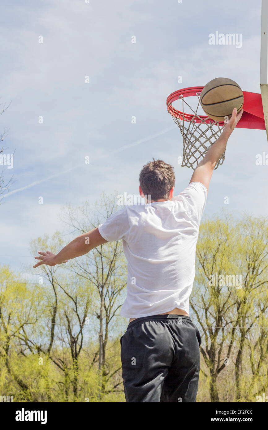 Jeune homme faisant le basket Trick Shots comme il saute en l'air Banque D'Images