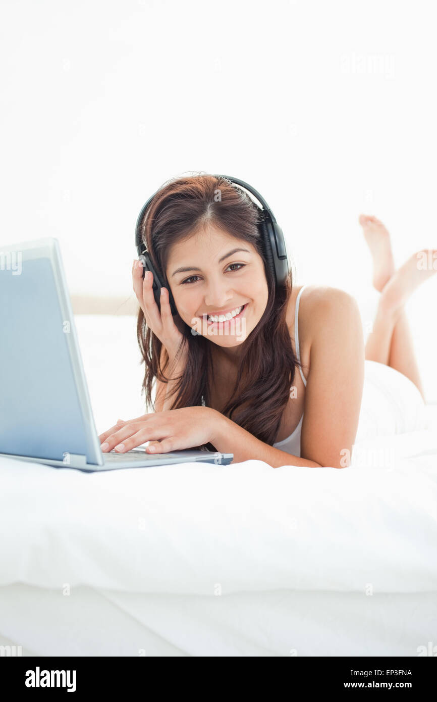 Femme avec casque et un coffre allongé sur lit, impatient et souriant Banque D'Images Femme avec casque et un coffre allongé sur lit, impatient et souriant Banque D'Images