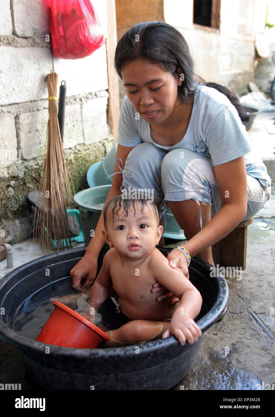Mère lave son fils (10 mois) dans une cuve en plastique. Township Paranaque, Manille, Philippines, Asie Banque D'Images