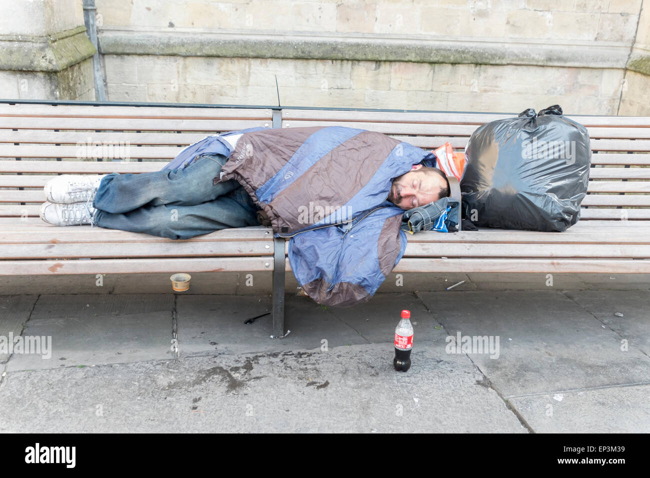 Une personne sans-abri dorment dans la rue sur un banc à Bath Somerset avec un sac d'effets personnels Banque D'Images