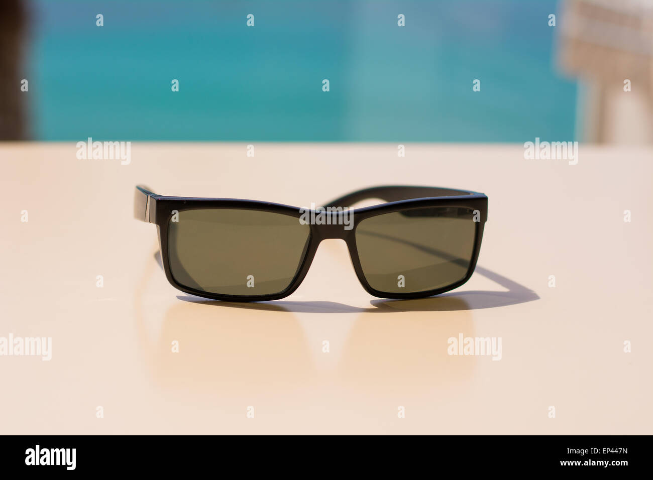 Une paire de lunettes de soleil sur une table avec un beau palmier et de la mer sur l'arrière-plan flou. L'été photo parfaite. Banque D'Images