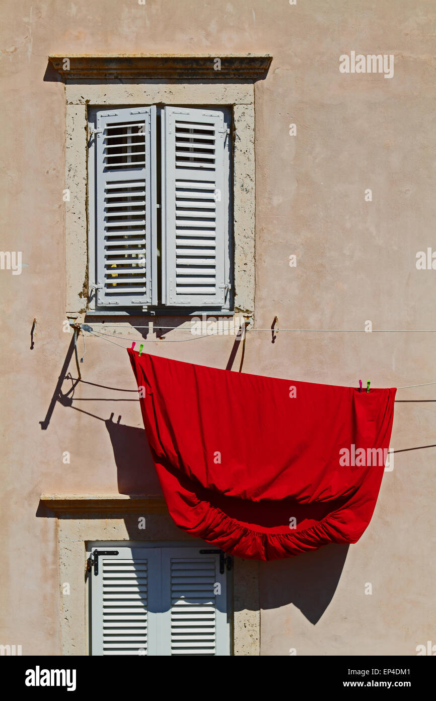 Drap de lit rouge suspendu à une fenêtre avec volets Banque D'Images