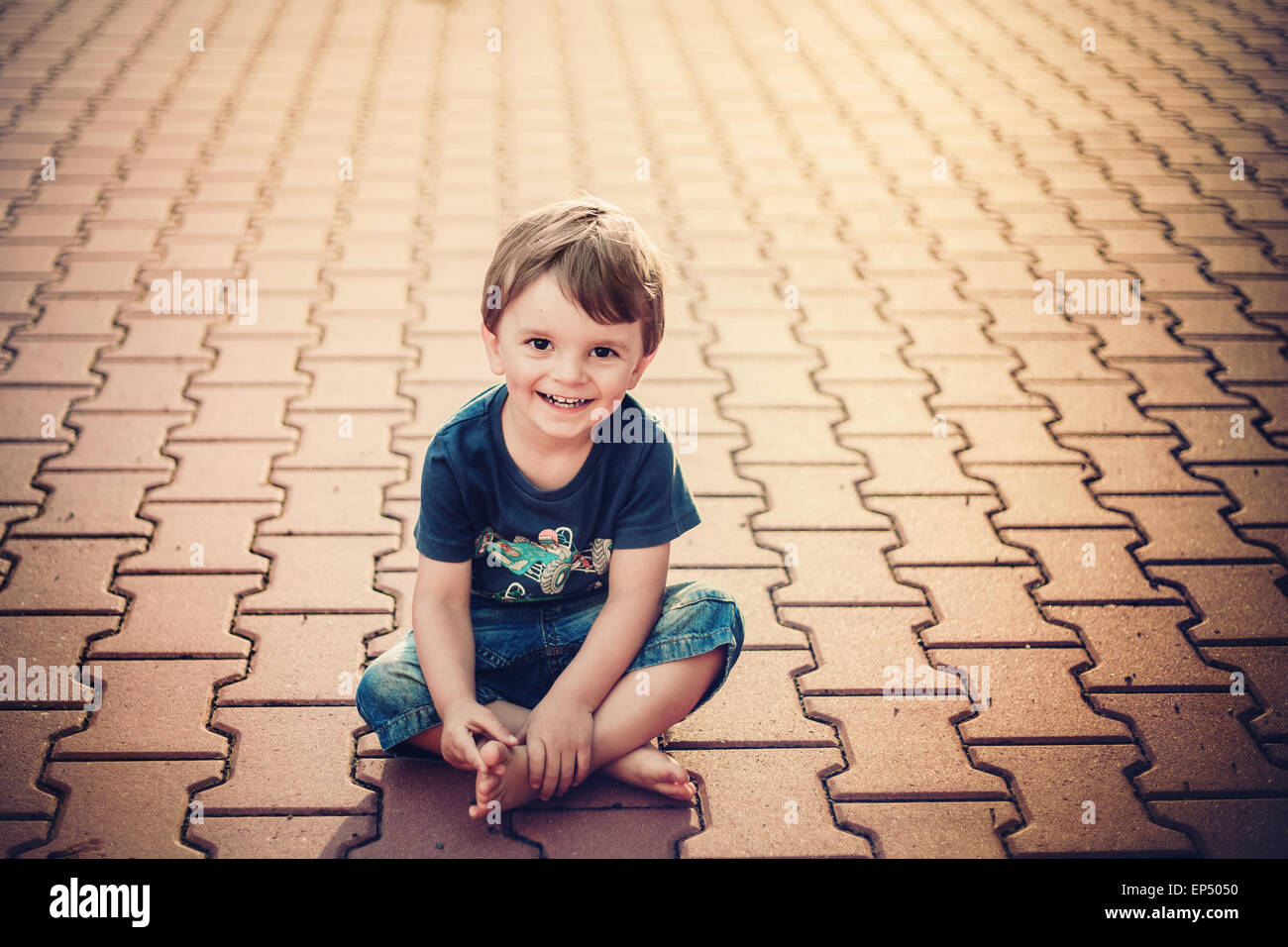 Smiling petit garçon assis sur le sol Banque D'Images