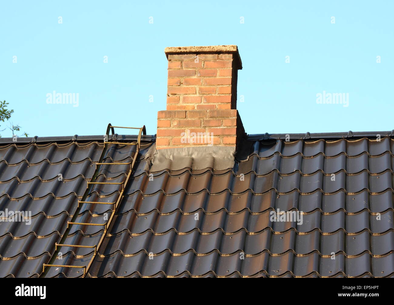 Cheminée en brique sur le toit noir avec échelle en métal Banque D'Images