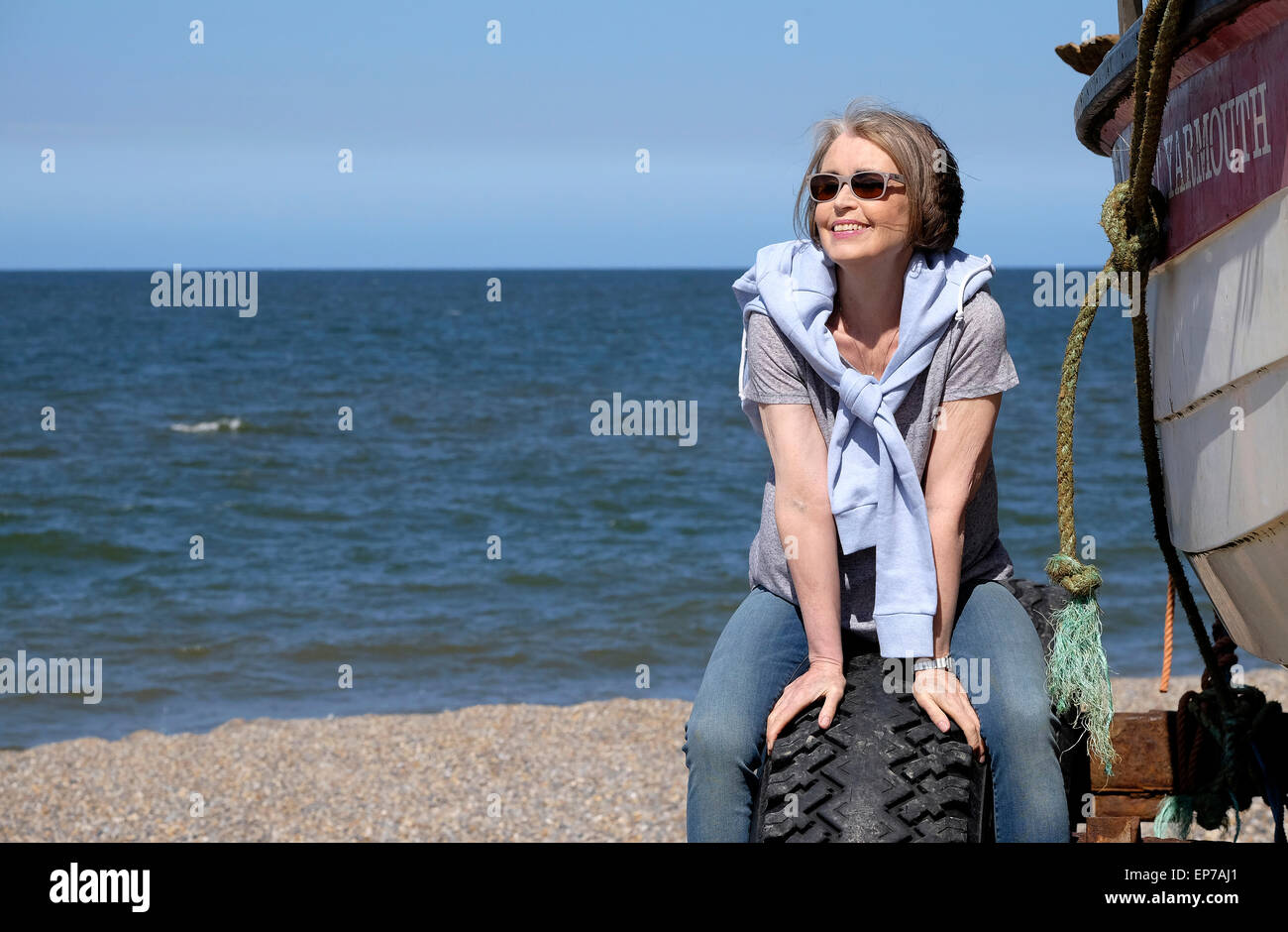 Senior woman sitting by fishing boat on beach Banque D'Images