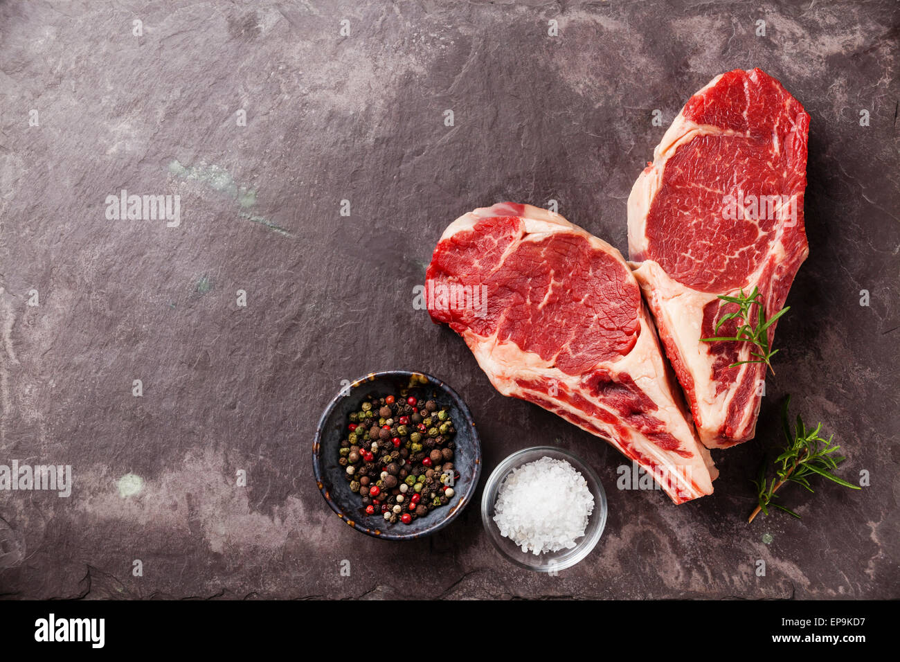 Forme de coeur matières la viande fraîche Ribeye Steak avec le romarin, le poivre et le sel sur fond ardoise Banque D'Images