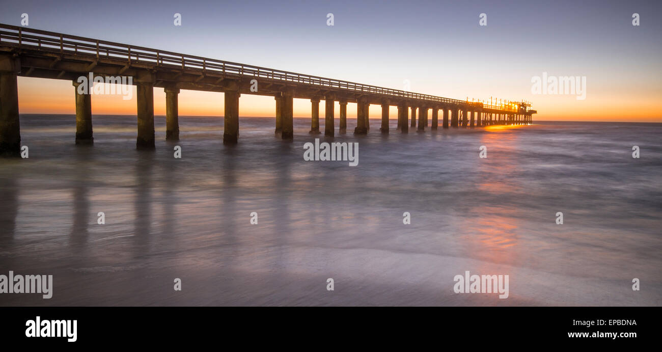 L'Afrique, la Namibie, l'Swokupmond. Bridge dans l'océan au coucher du soleil avec des vagues se brisant sur le rivage. Banque D'Images