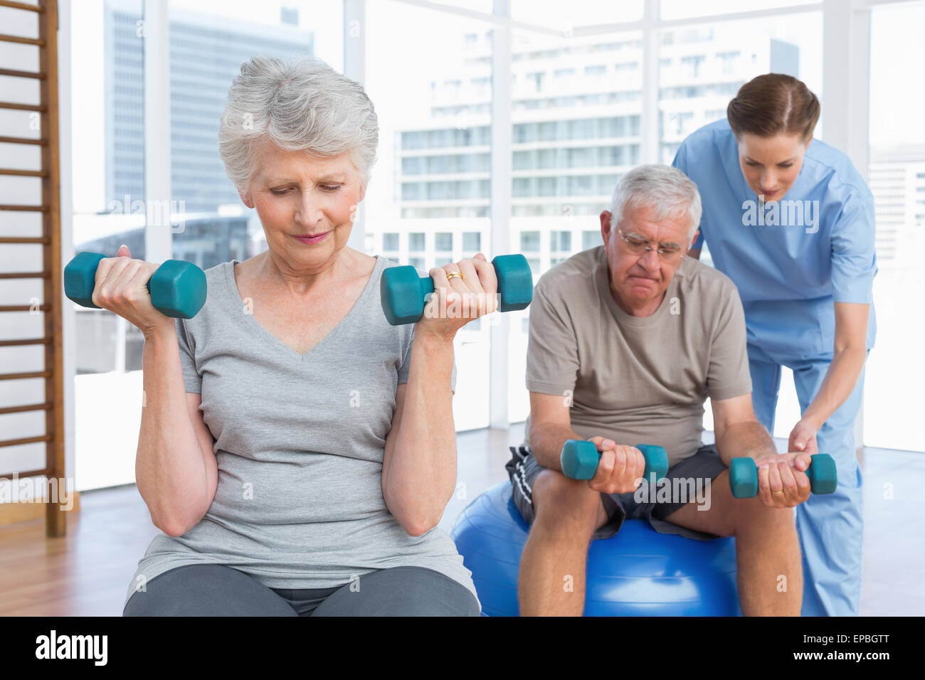 Female therapist aider senior couple with dumbbells Banque D'Images